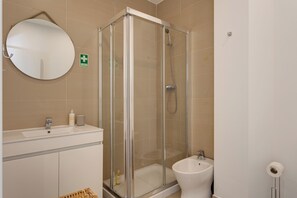 A bathroom with a glass-enclosed shower, a round mirror, a sink, and a bidet. - Baixa Garden: 2BR + Patio | Perfect for Families (Lisboa)
