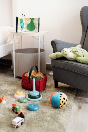 Ein Spielbereich für Kinder mit Spielzeug, einem Korb und einem grauen Sessel.