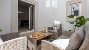 Eine sonnendurchflutete Terrasse mit Korbmöbeln, einem Tisch mit Tellern und Getränken und Blick in den angrenzenden Raum.