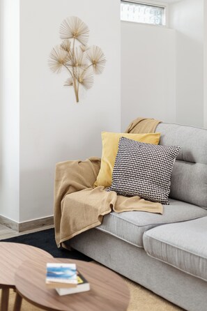 Un salon avec un canapé gris, un plaid jaune, un coussin à motifs et un élément décoratif fixé au mur.