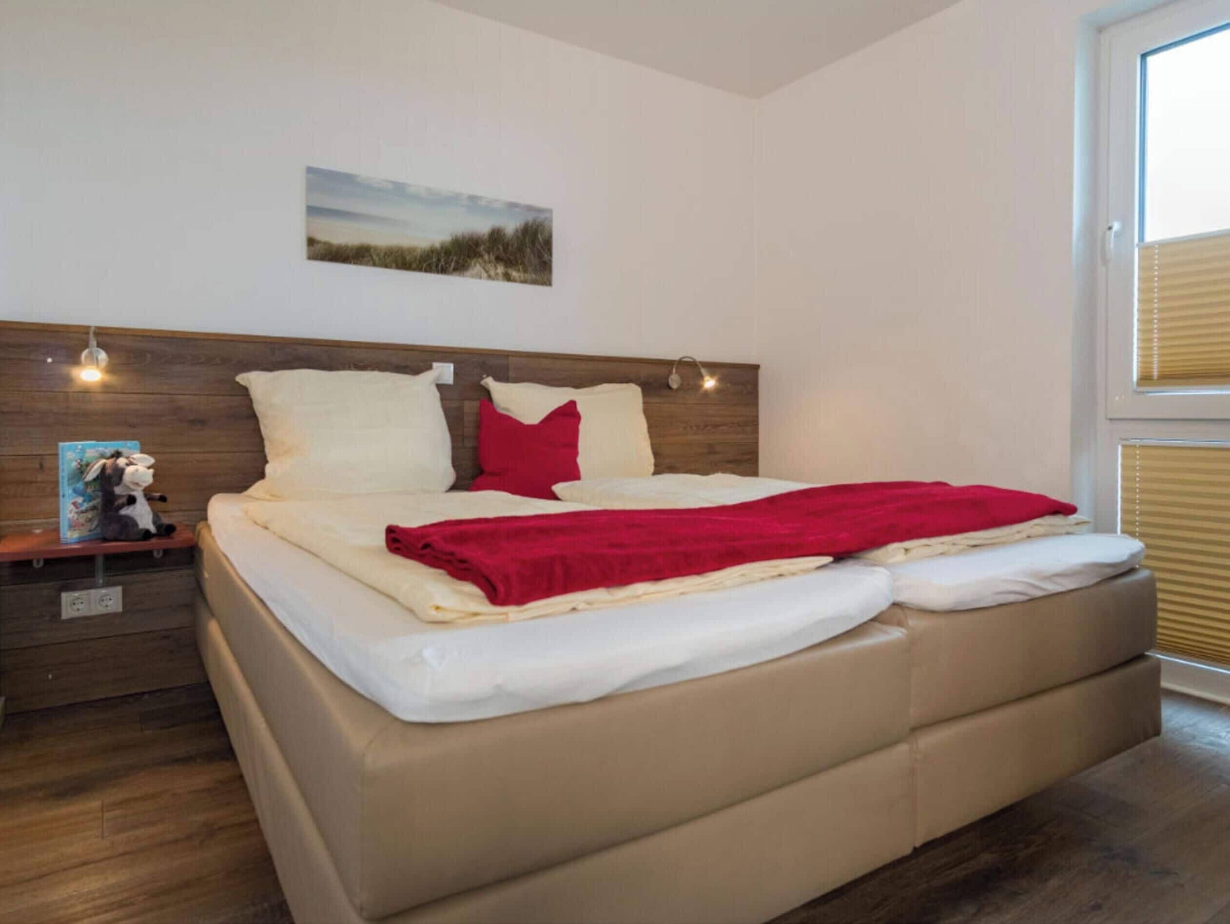 A bedroom with a bed, a nightstand, a wall-mounted light, and a window with blinds.