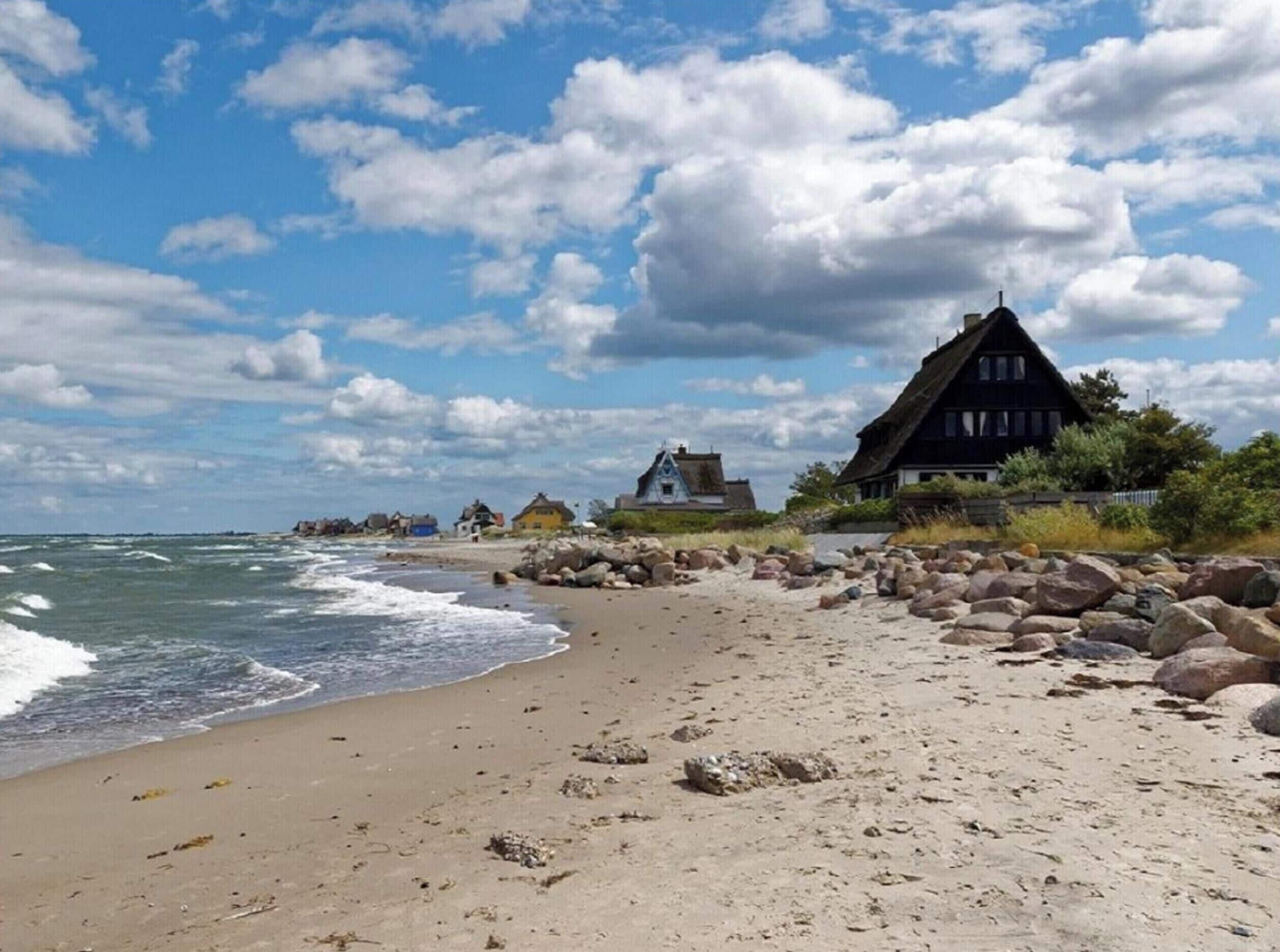 A beach with a row of traditional houses, a rocky shoreline, and waves crashing onto the sand.