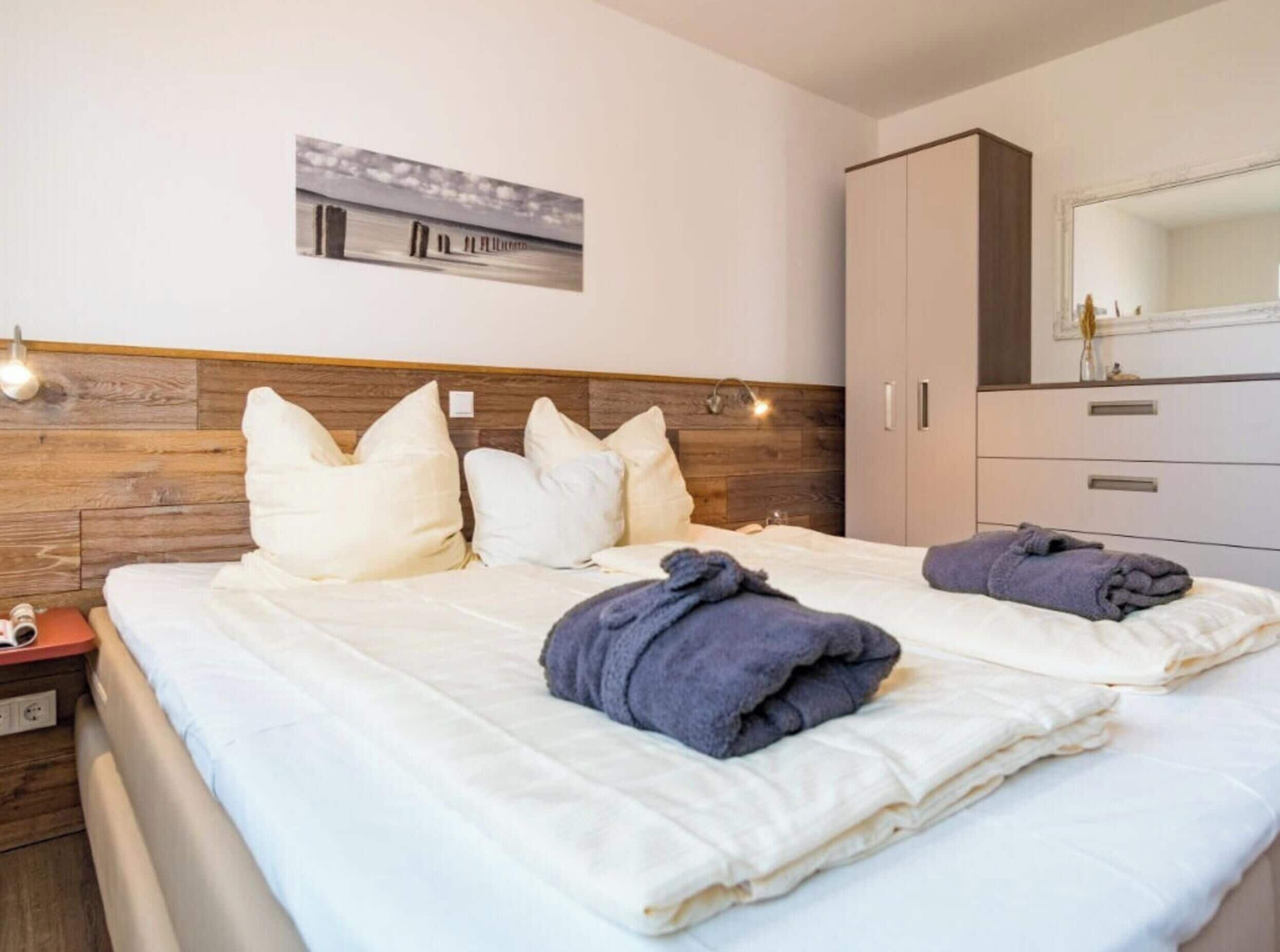 A hotel room with a bed, pillows, a nightstand, a wardrobe, and a mirror.