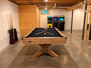 Ein Billardtisch mit Billardstöcken und Kugeln, Spielautomaten und eine Holzwand.
