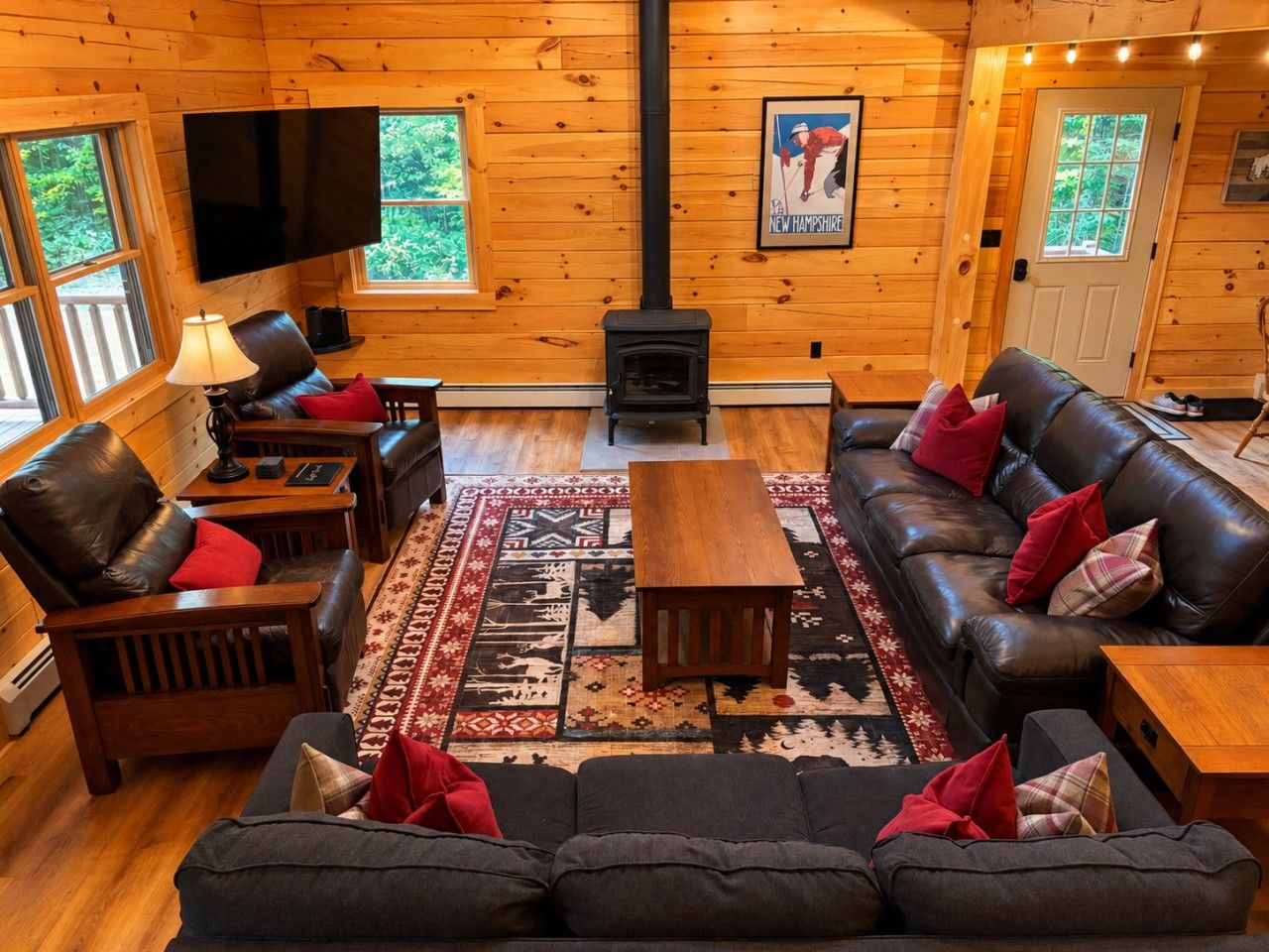 Un intérieur de chalet chaleureux avec une cheminée, des canapés en cuir, un téléviseur à écran plat et une grande fenêtre.