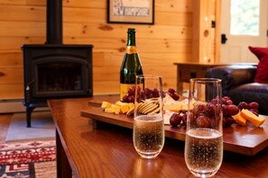 Una mesa de madera con una botella, vasos, queso y uvas.