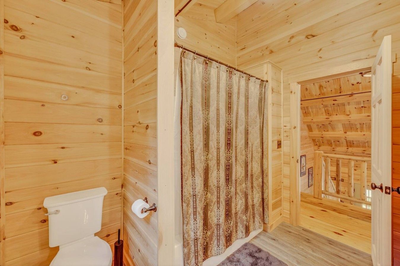 En stuga med träpanel på insidan, en toalett, ett mönstrat draperi och en trappa som leder upp till en veranda.