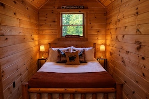Ein gemütliches Schlafzimmer in einer Holzhütte mit Bett, Kissen und einem Fenster.