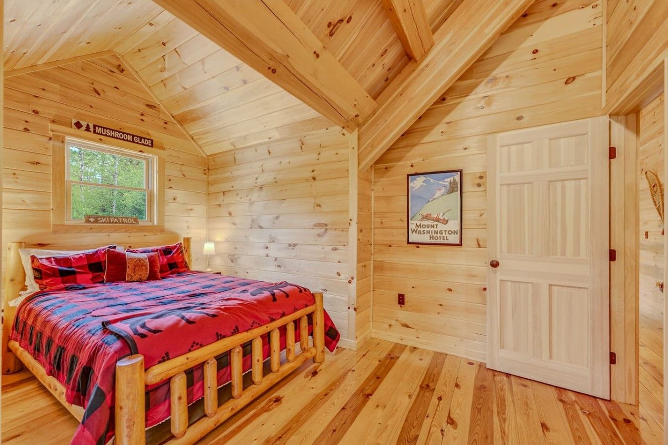 Een houten kamer met een bed, een raam, een deur en een poster aan de muur.