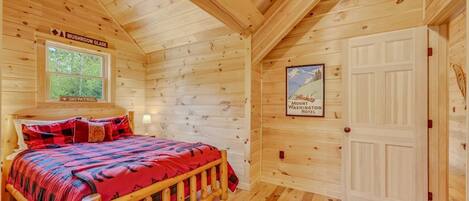 A wooden cabin room with a bed, a window, a door, and a poster on the wall.