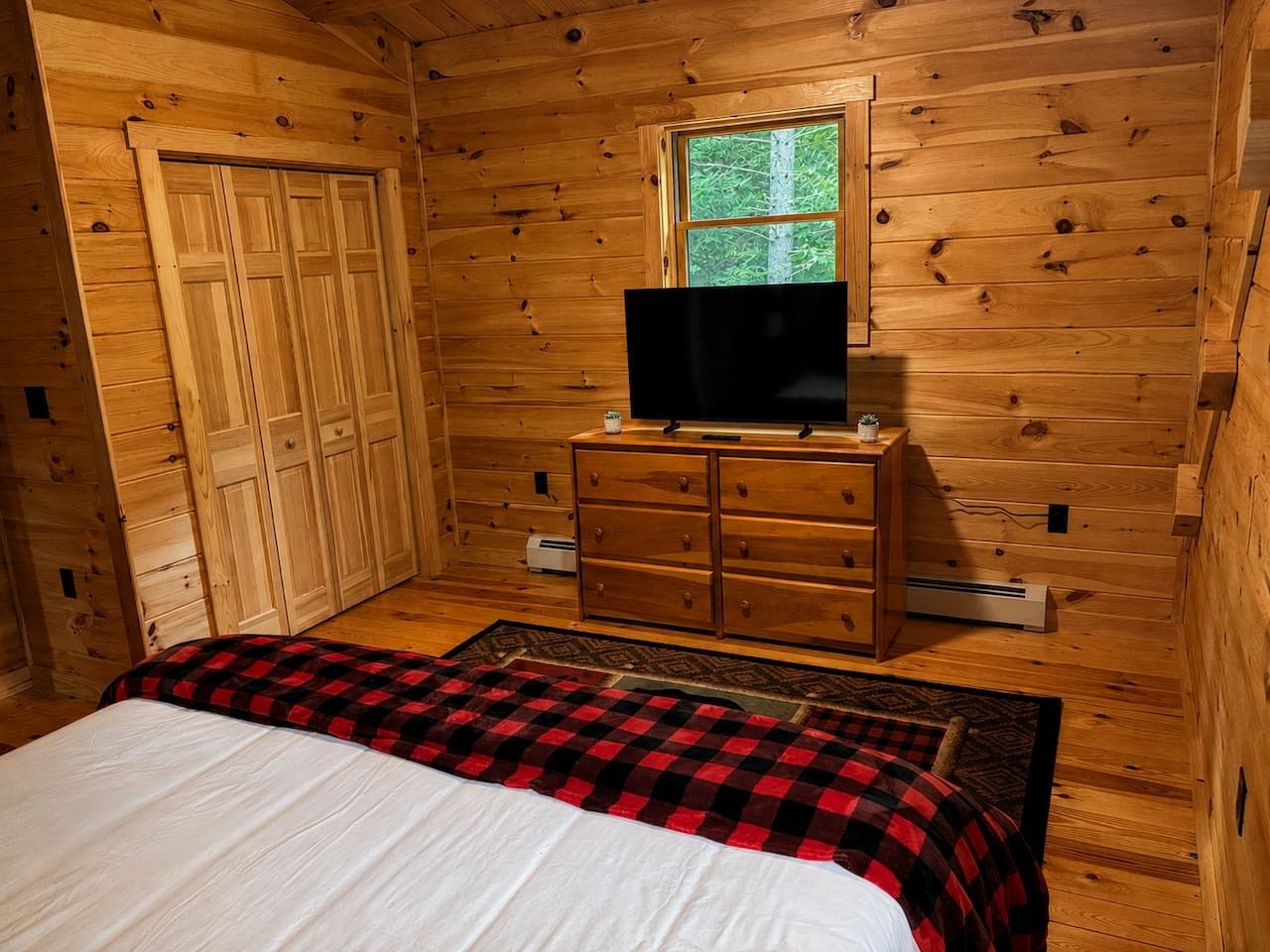 Habitación de cabaña de madera con cama, cómoda y televisión.
