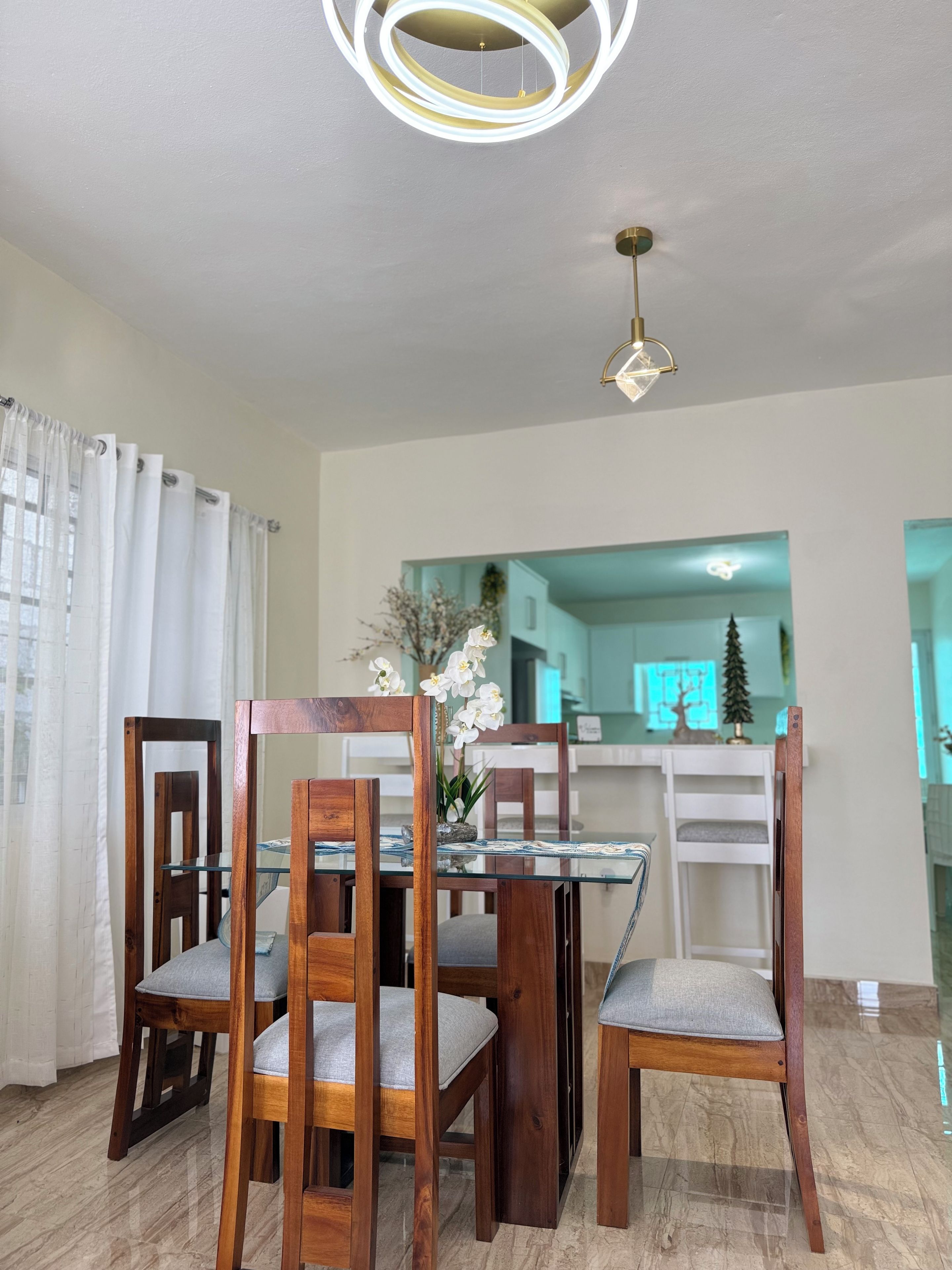 Un comedor con una mesa de vidrio, sillas de madera y una lámpara moderna en el techo.