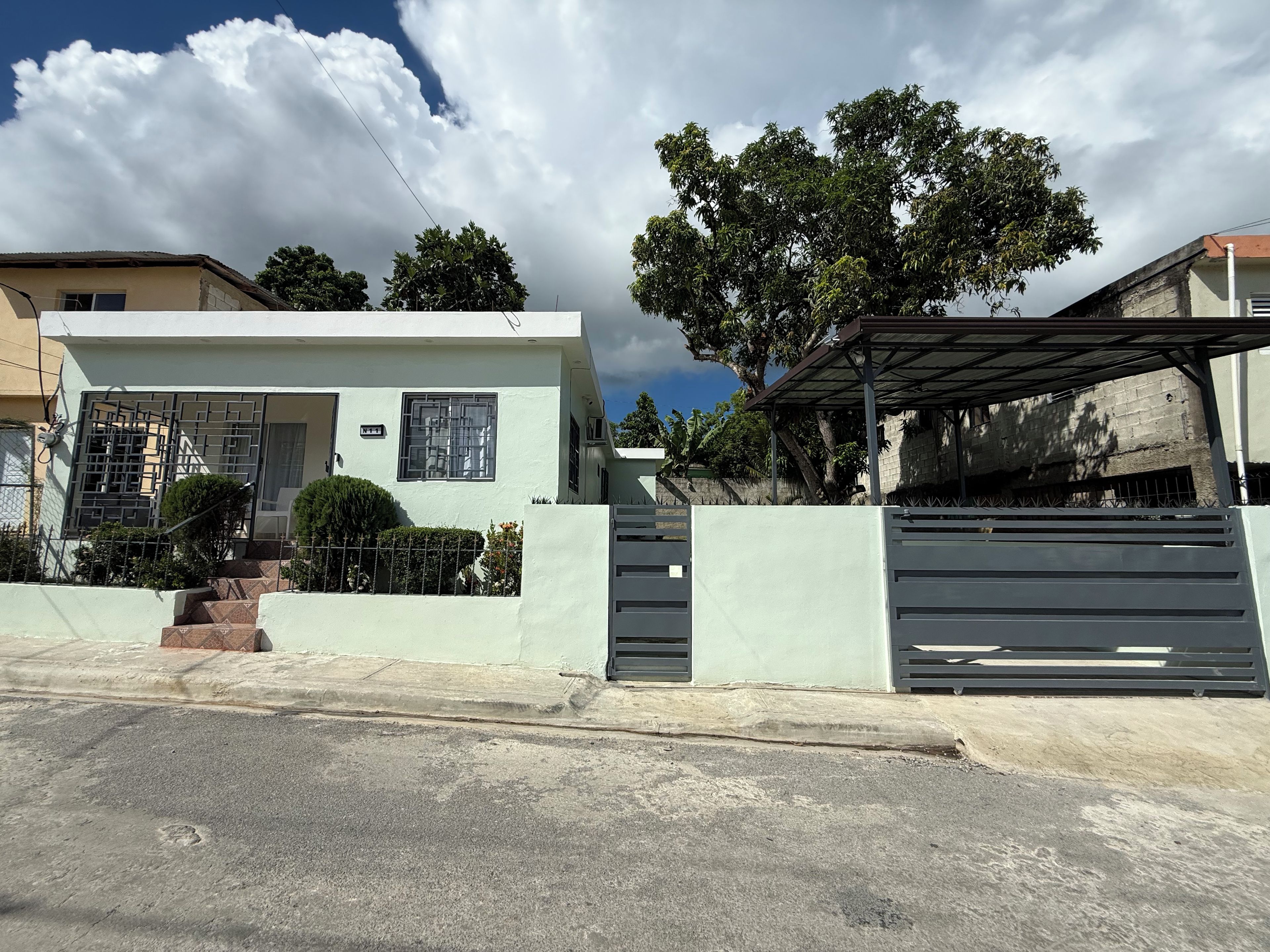 Un edificio residencial con entrada protegida por un portón, un porche cubierto y una escalera que lleva a la entrada.