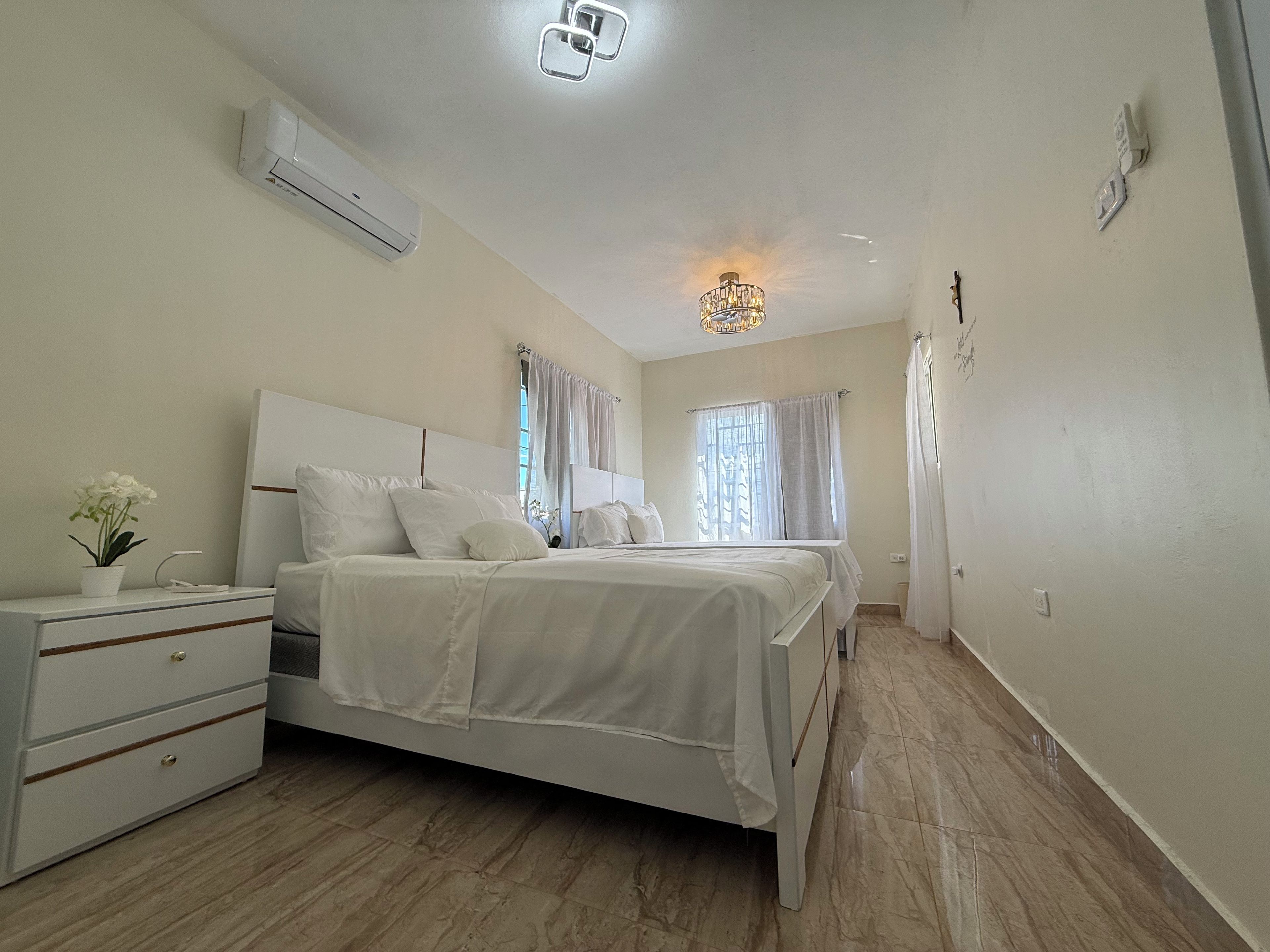 Un dormitorio con cama, mesitas de noche, cómoda y aire acondicionado, además de un candelabro.
