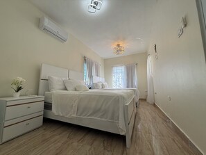 A bedroom with a bed, bedside tables, a dresser, an air conditioning unit, and a chandelier.
