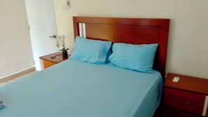 A bed with a wooden headboard, two pillows, a nightstand, and a bedside table with a lamp.