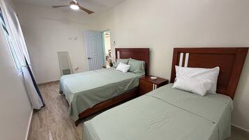 A hotel room with two beds, a ceiling fan, and a door leading to a bathroom.