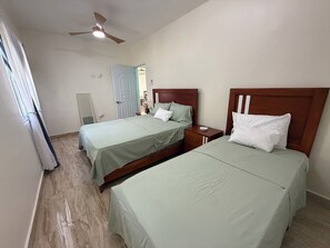 Ein Hotelzimmer mit zwei Betten, einem Deckenventilator und einer Tür zu einem Badezimmer.