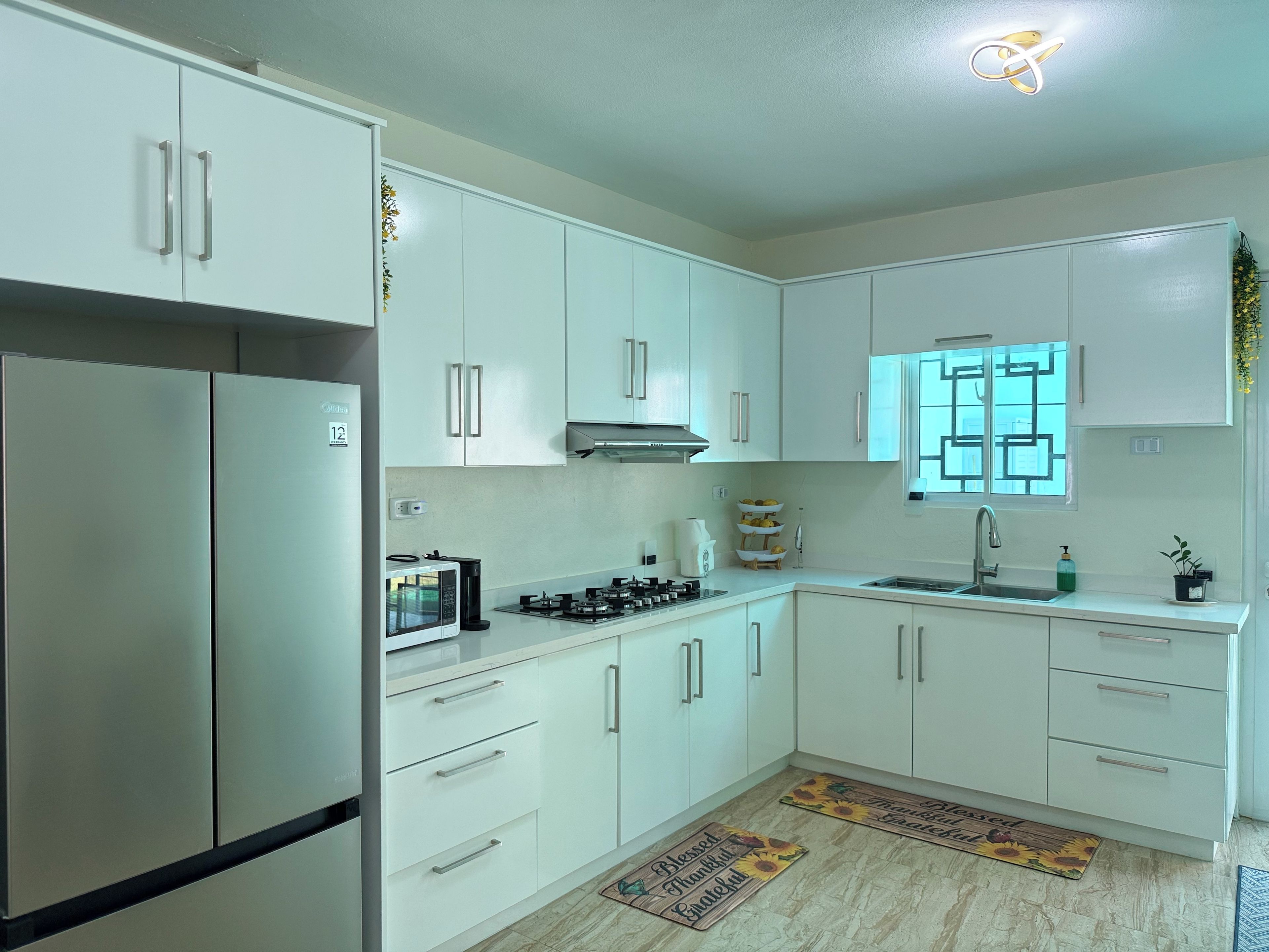 A modern kitchen with white cabinets, stainless steel appliances, and a window with a geometric pattern.