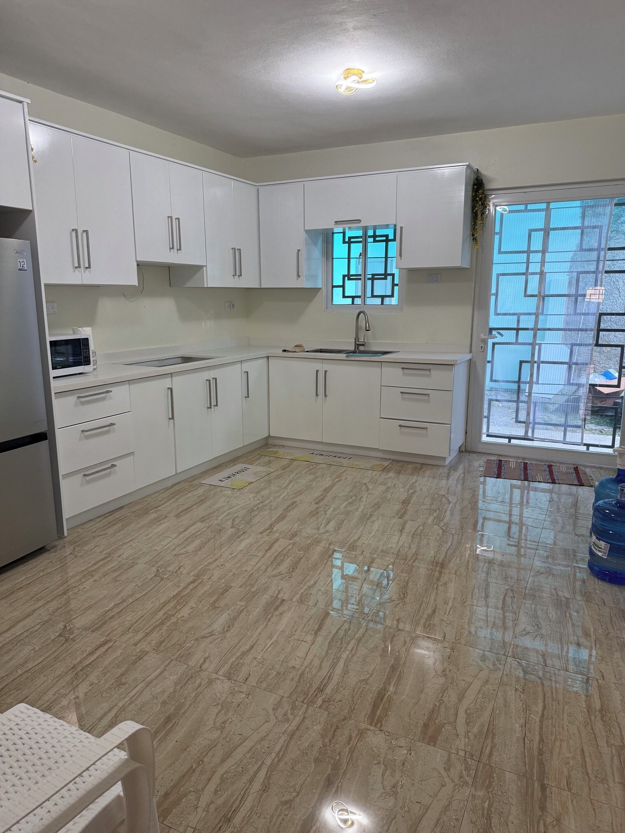 Una cocina con gabinetes blancos, un refrigerador de acero inoxidable, un microondas y un fregadero.