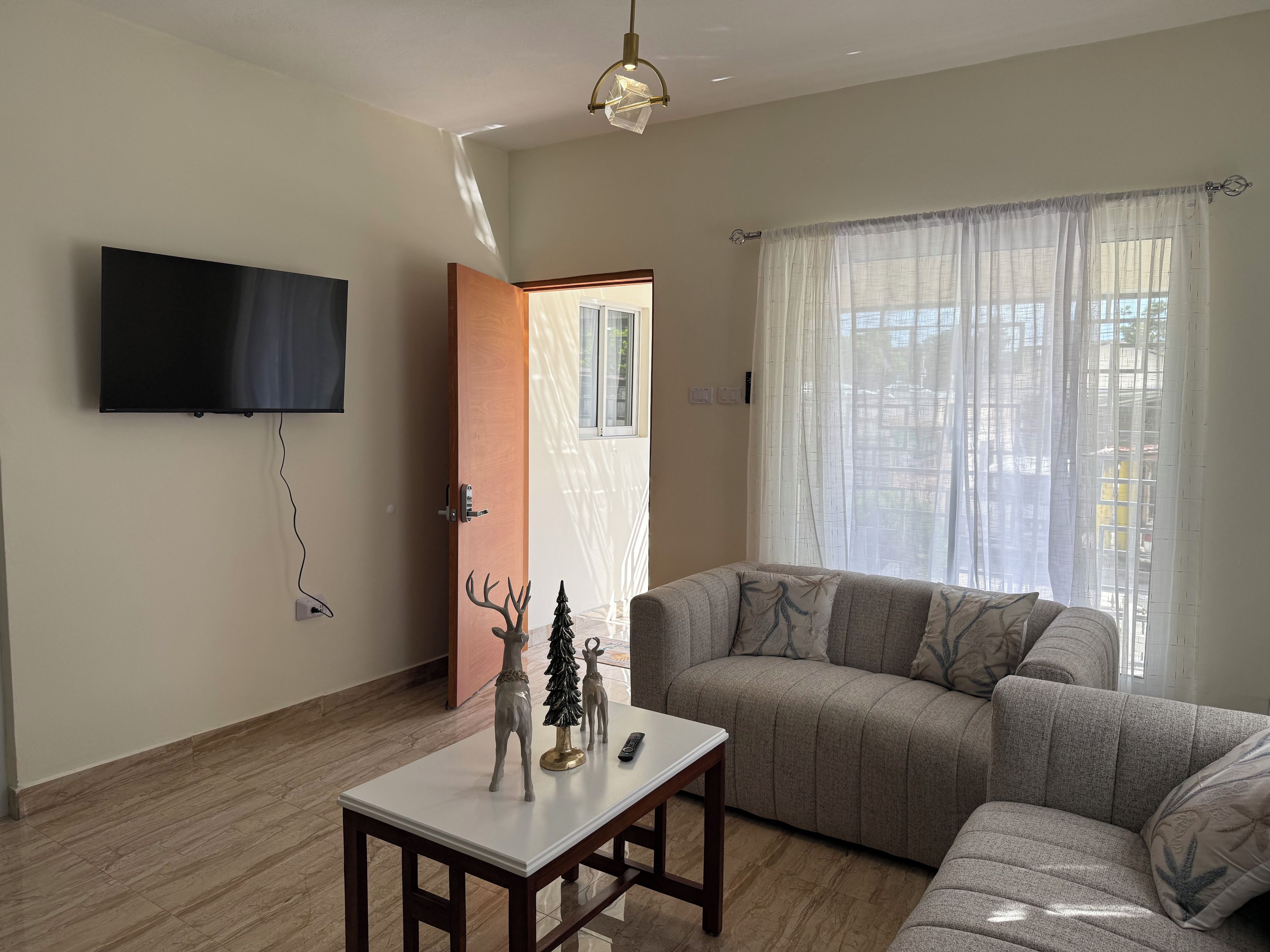 Ein Wohnzimmer mit einer Couch, einem Couchtisch, einem an der Wand befestigten Fernseher und einem Fenster mit Vorhängen.