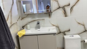 Une salle de bain avec un mur en marbre, un lavabo, des toilettes et un miroir.