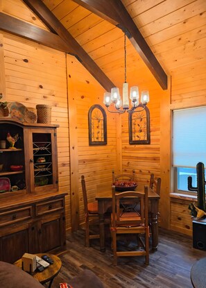 A wooden interior with a dining table, chairs, a chandelier, and a cabinet with decorative items. - Cozy 2bdrm, 1 bath cabin right in the middle of the Bitterroot Valley. (Victor)