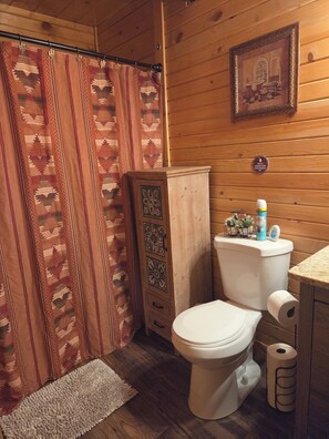 A wooden bathroom with a toilet, a cabinet, a shower curtain, and a framed picture on the wall. - Cozy 2bdrm, 1 bath cabin right in the middle of the Bitterroot Valley. (Victor)