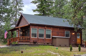 A log cabin with a porch, windows, and an American flag. - Cozy 2bdrm, 1 bath cabin right in the middle of the Bitterroot Valley. (Victor)