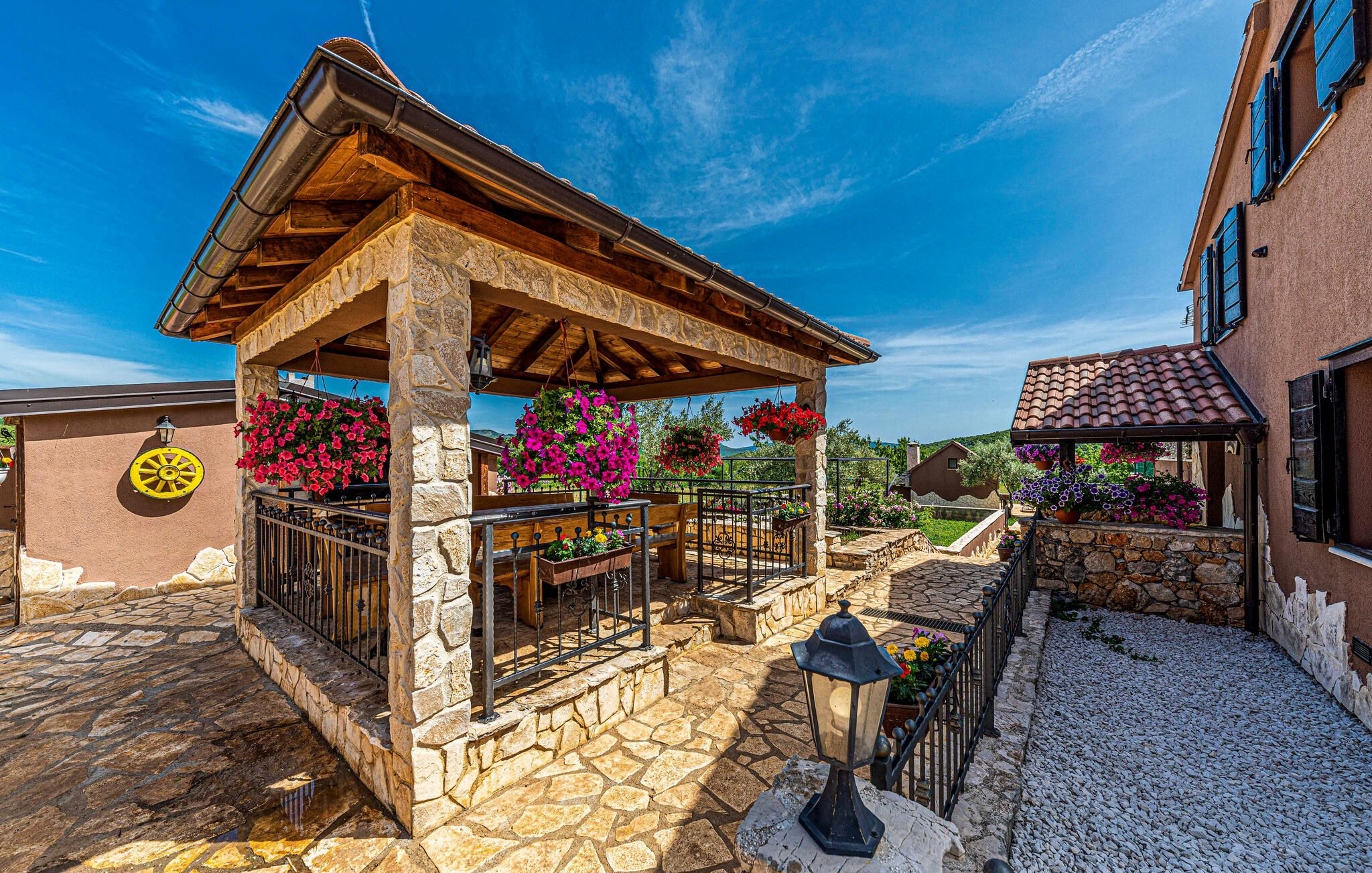 Une cour pavée de pierres, agrémentée d’une pergola en bois, de murs en pierre et de jardinières suspendues.