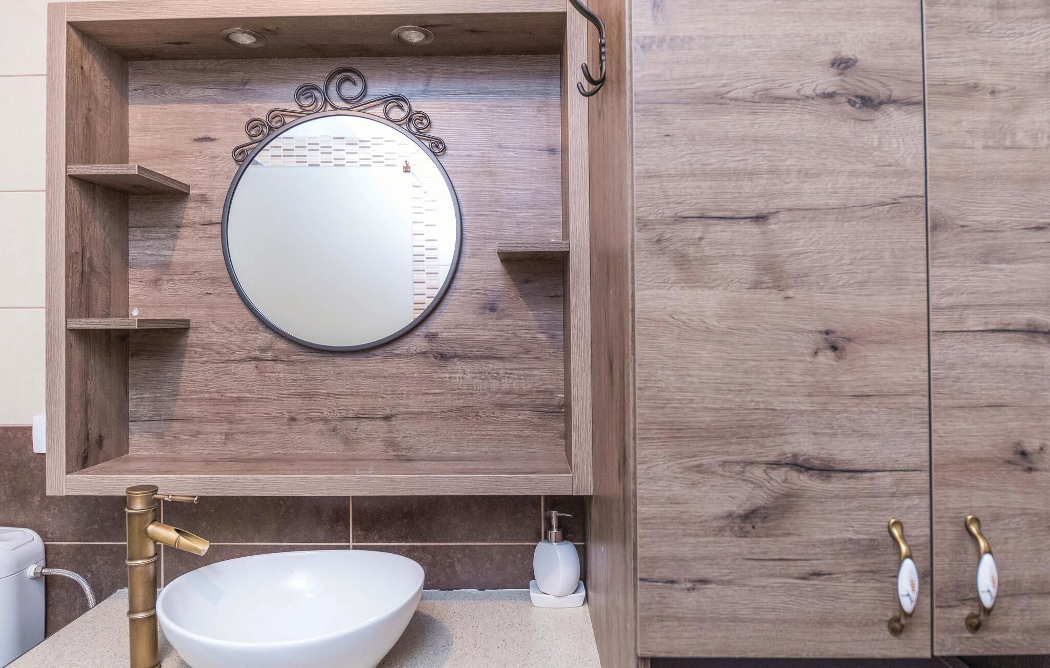 Une salle de bain avec un meuble-lavabo en bois, un miroir rond, un lavabo blanc et un robinet en laiton.