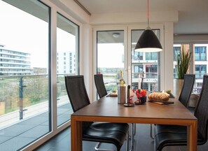 Ein moderner Essbereich mit einem Holztisch, schwarzen Stühlen und einem großen Fenster mit Blick auf die Stadt.