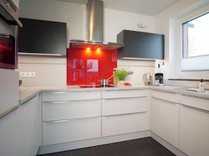 Eine moderne Küche mit weißen Schränken, einer roten Spritzschutzwand und Edelstahlgeräten.
