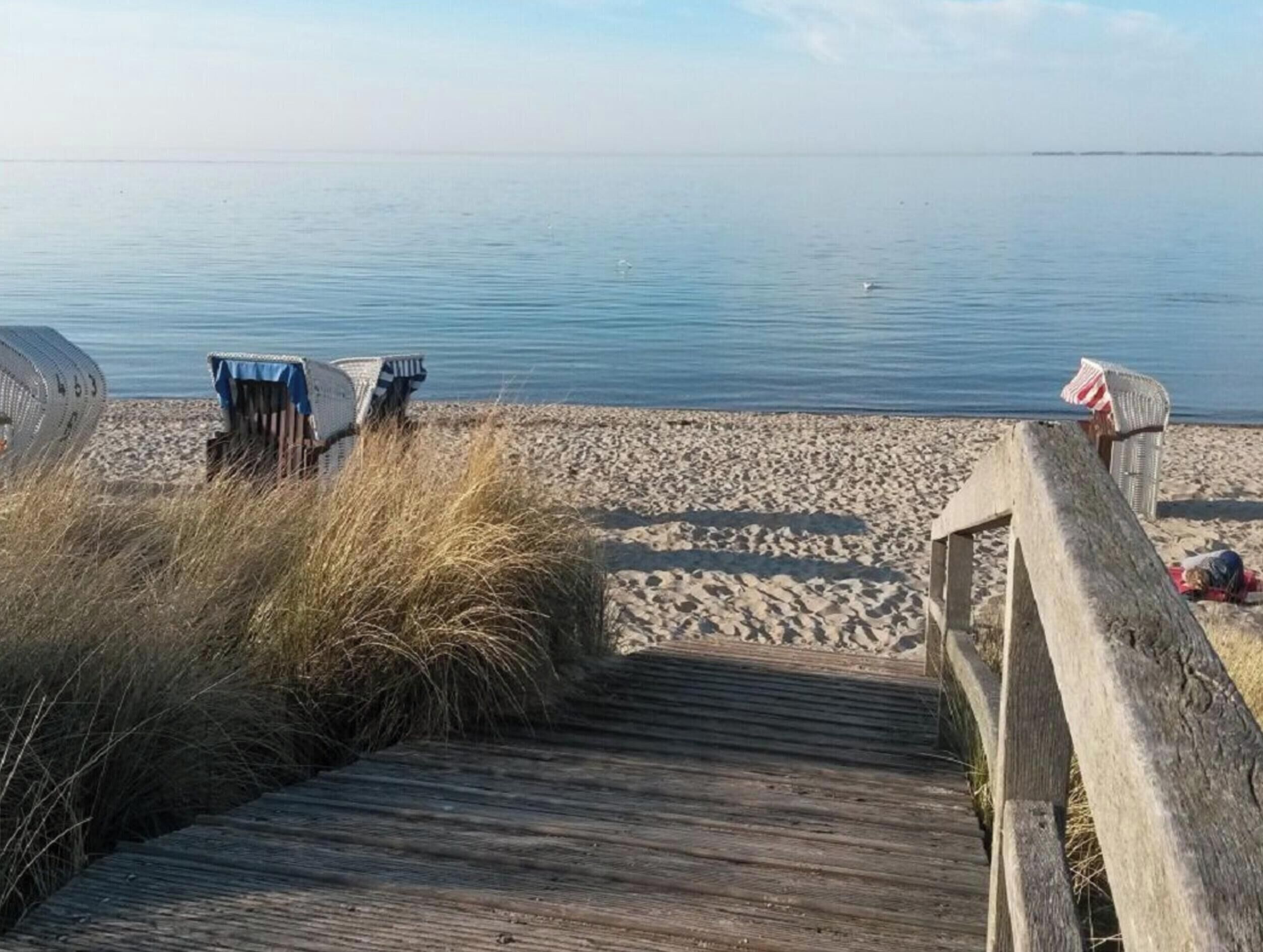 A wooden boardwalk leading to a sandy beach with calm water in the background.
