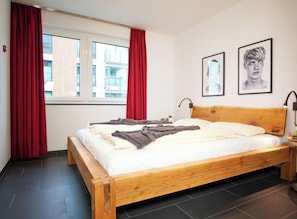 Une chambre à coucher avec un lit en bois, des rideaux rouges, une fenêtre et deux tableaux encadrés accrochés au mur.