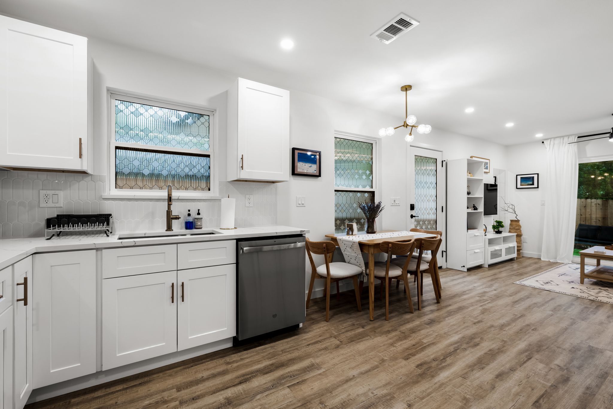 A modern kitchen with white cabinetry, a dishwasher, and a dining area with a table and chairs.