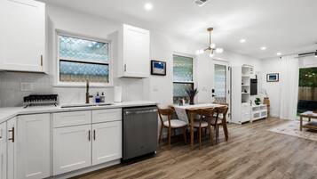 A modern kitchen with white cabinetry, a dishwasher, and a dining area with a table and chairs.