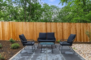 An outdoor patio with two black metal chairs and a table, surrounded by a wooden fence and greenery. - Newly Built South Austin 2BR Guesthouse - Quiet & Modern (Austin)