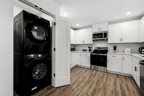 Una cocina moderna con armarios blancos, horno de acero inoxidable, microondas y una lavadora Samsung negra.