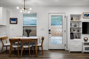 Un'area pranzo con un tavolo rotondo e quattro sedie, un armadietto bianco con ripiani e una porta con pannelli di vetro decorativi.