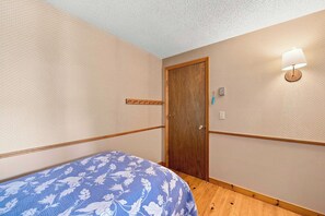A room with a wooden door, a bed with a floral bedspread, a wall-mounted light, and a textured wall. - Center Harbor Lake Escape | Private Dock (Center Harbor)