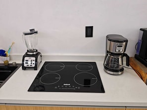 A kitchen with an induction cooktop, a coffee maker, and a blender on a white countertop.