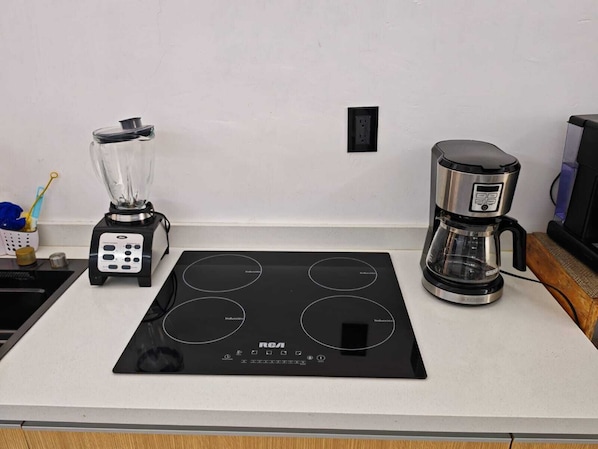 A kitchen with an induction cooktop, a coffee maker, and a blender on a white countertop.