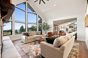 A spacious living room with large windows, a fireplace, and a view of the outdoors. - Hilltop Retreat | Indoor Pickleball | Event Arena (Corvallis)