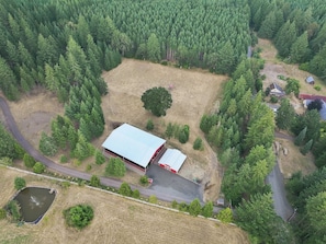 An aerial view of a property with a large open field, a fenced area, a building with a red roof, and a road. - Hilltop Retreat | Indoor Pickleball | Event Arena (Corvallis)