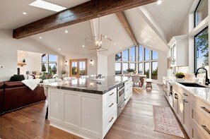 A spacious kitchen with a large island, wooden beams, and large windows. - Hilltop Retreat | Indoor Pickleball | Event Arena (Corvallis)