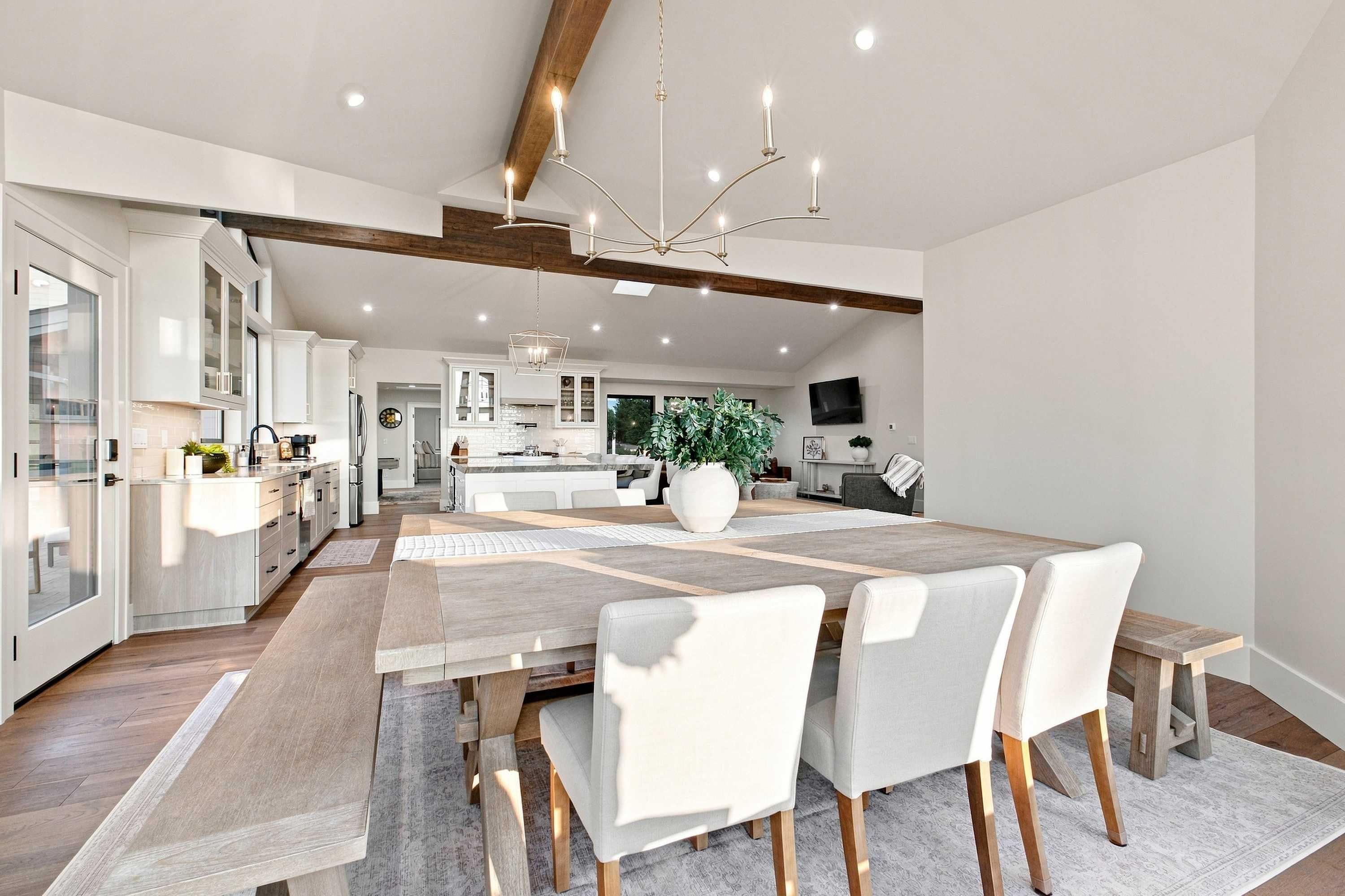 A modern kitchen with white cabinets, a central island, and a dining area with a large table and chairs.
