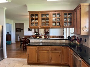 A kitchen with wooden cabinets, a black countertop, and a dining area with chairs and a table.