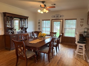 A dining room with a wooden table, chairs, a ceiling fan, and a kitchen area with a bar stool.