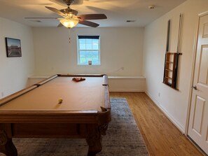 A pool table in a room with a ceiling fan, a window, and a door with a shelf.